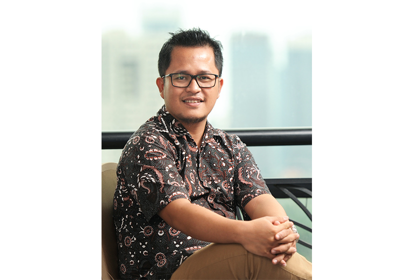 A man with glasses wearing black batik shirt sitting on the sofa